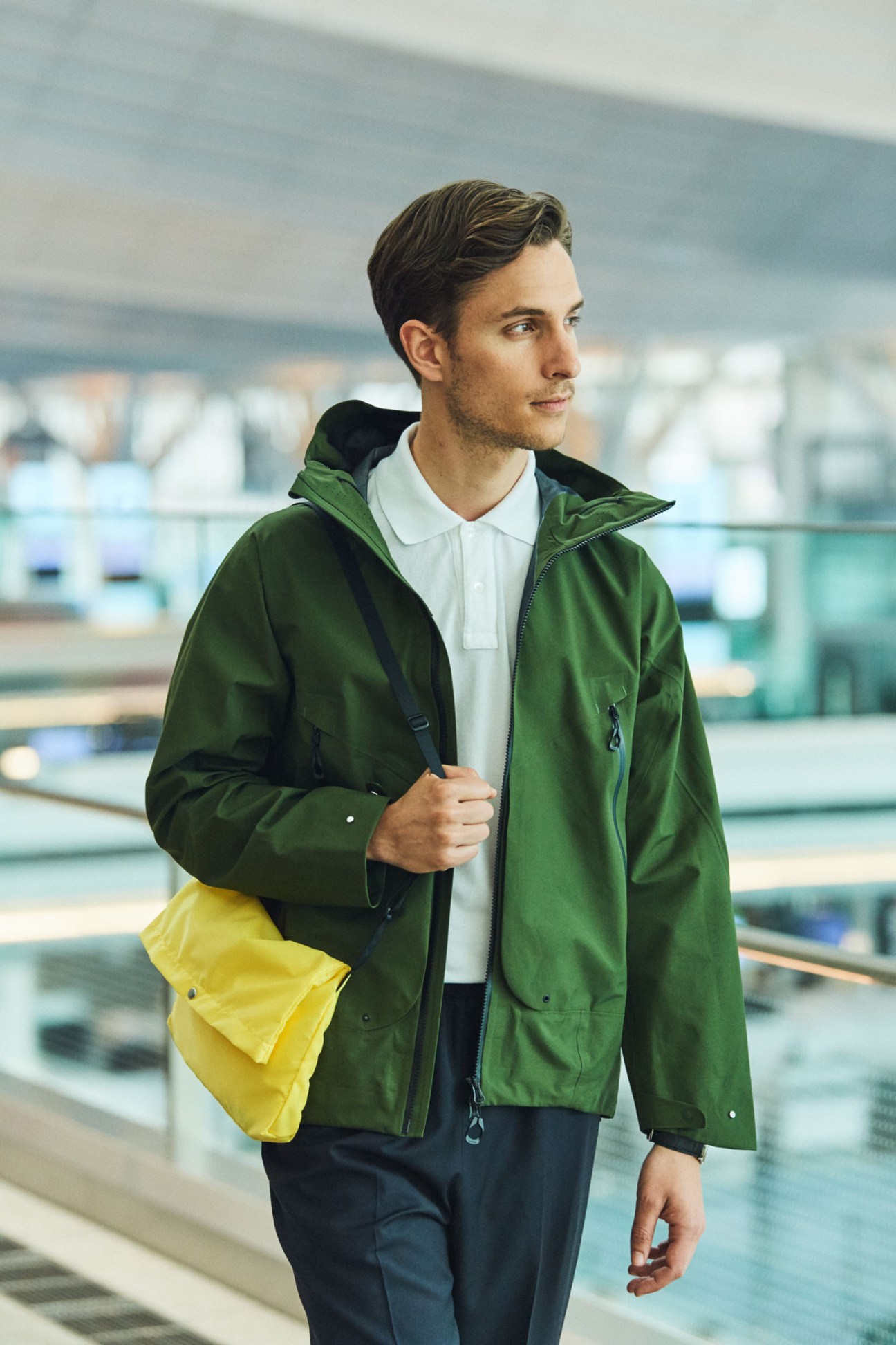 Man wearing green Goldwin jacket and yellow bag at Tokyo airport terminal window