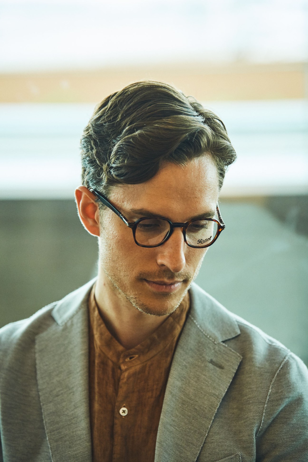 Man wearing Eleventy jacket and Brooksfield shirt with Persol glasses looking downward.