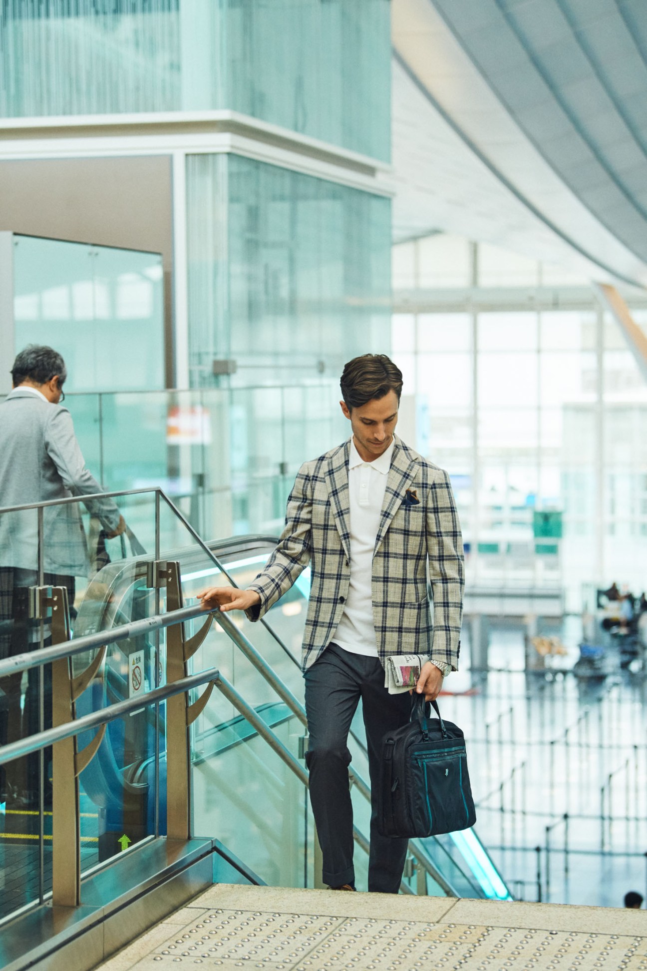 Man in plaid jacket walking down stairs at airport holding a Victorinox bag