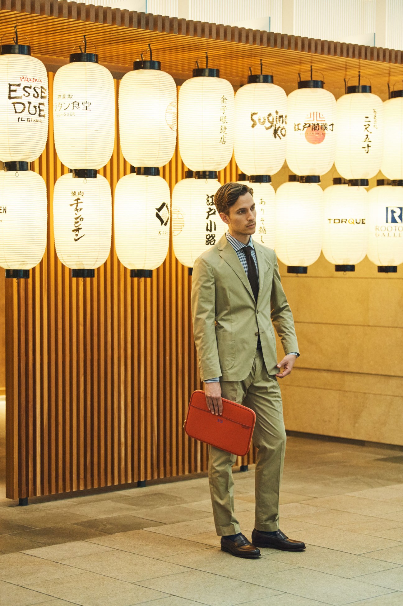 Man in tailored suit and laptop case standing at Tokyo International Airport.