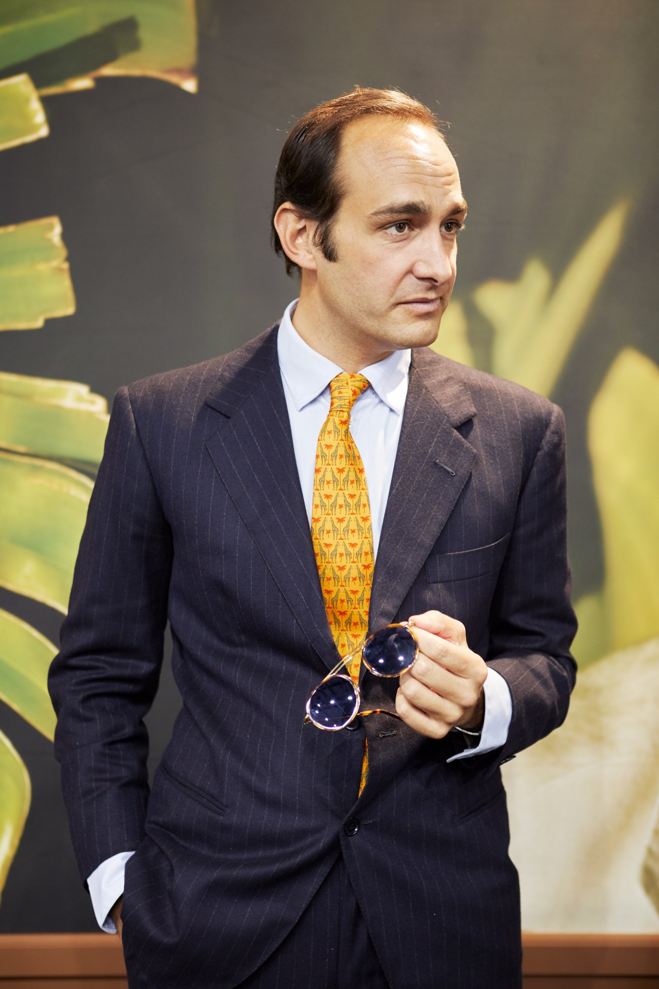 Luca Gnecchi Ruscone, owner of LGR, wearing a dark pinstriped suit and gold patterned tie, holding sunglasses at Mido eyewear trade show.