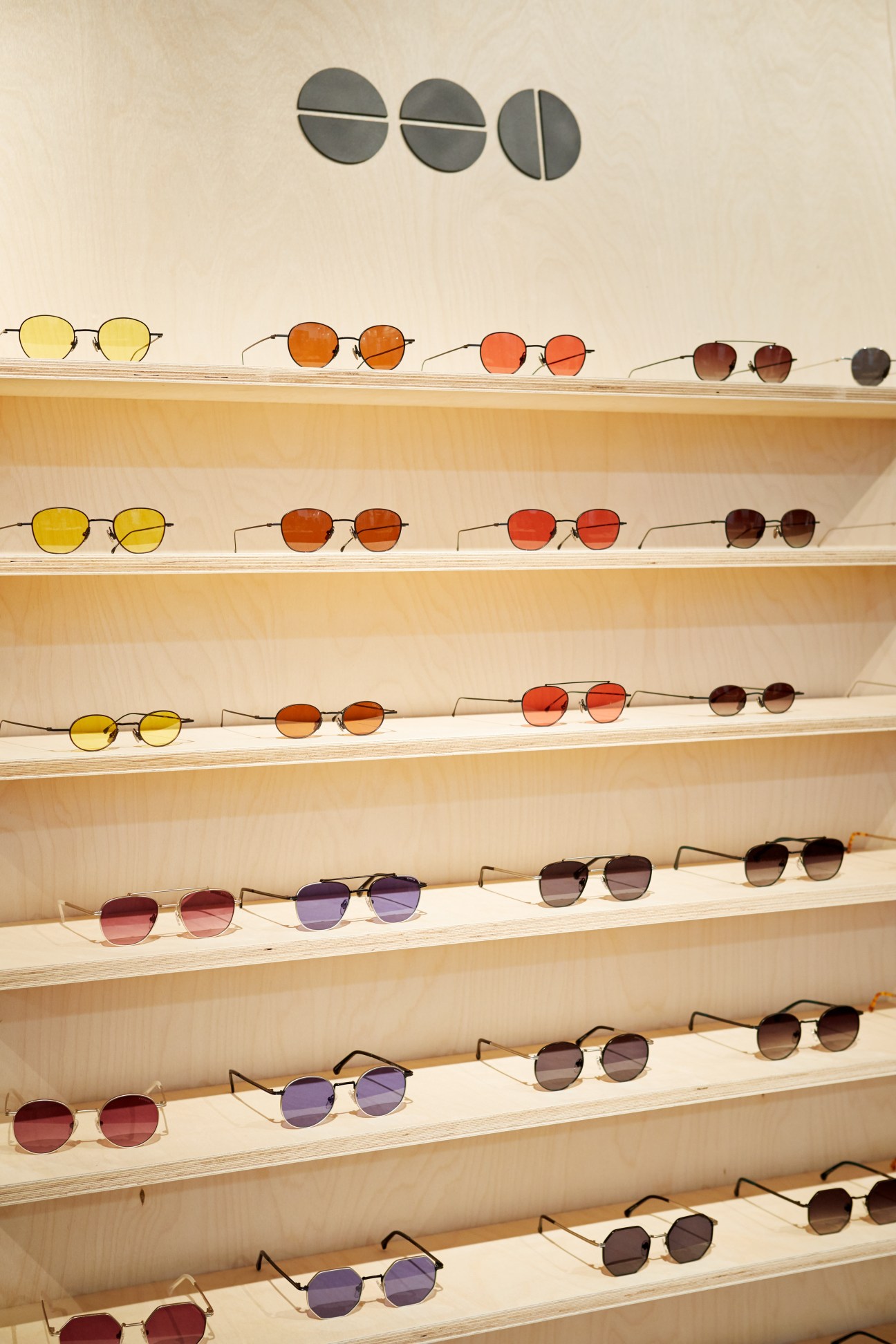 Wooden shelves displaying Komono sunglasses in various colored lenses arranged by shade gradient.