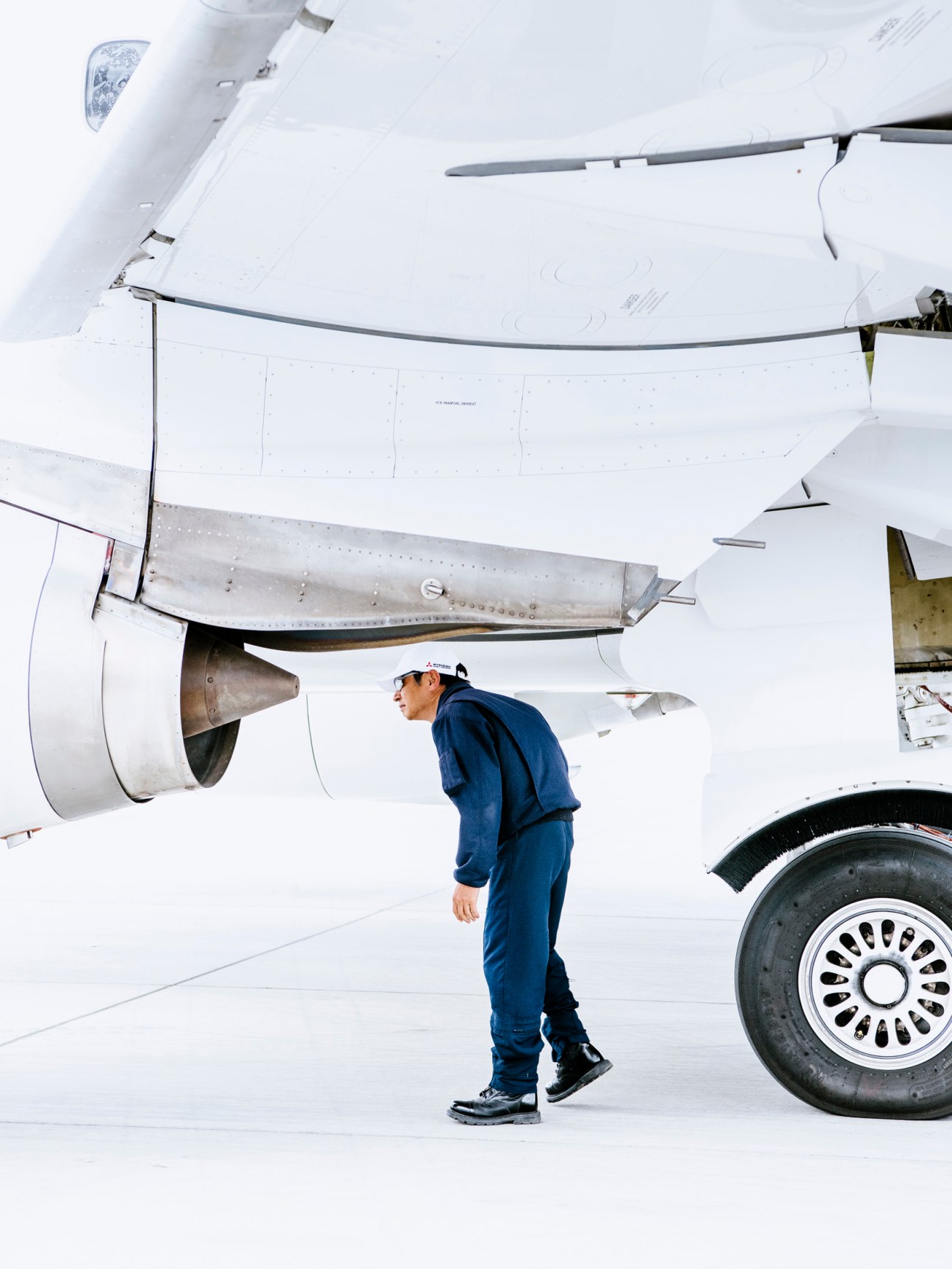 Aircraft maintenance technician in blue coveralls conducting walkaround inspection of white SpaceJet M90