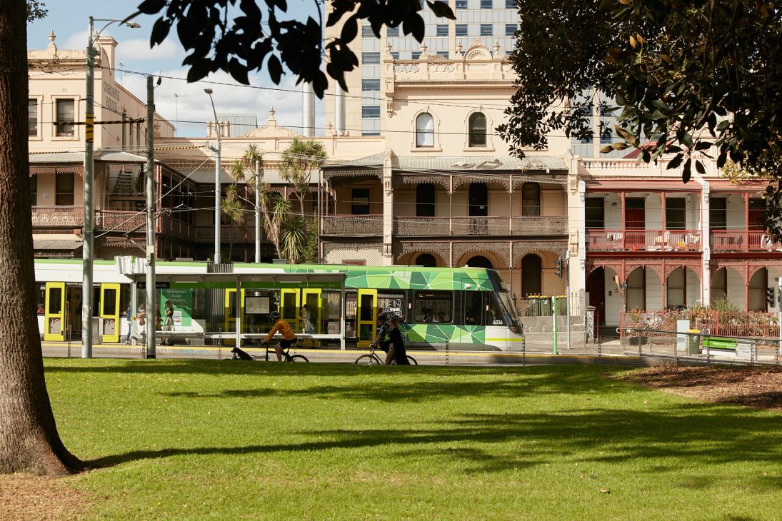 Green and yellow electric tram passes colonial-era buildings in Melbourne's urban streetscape.