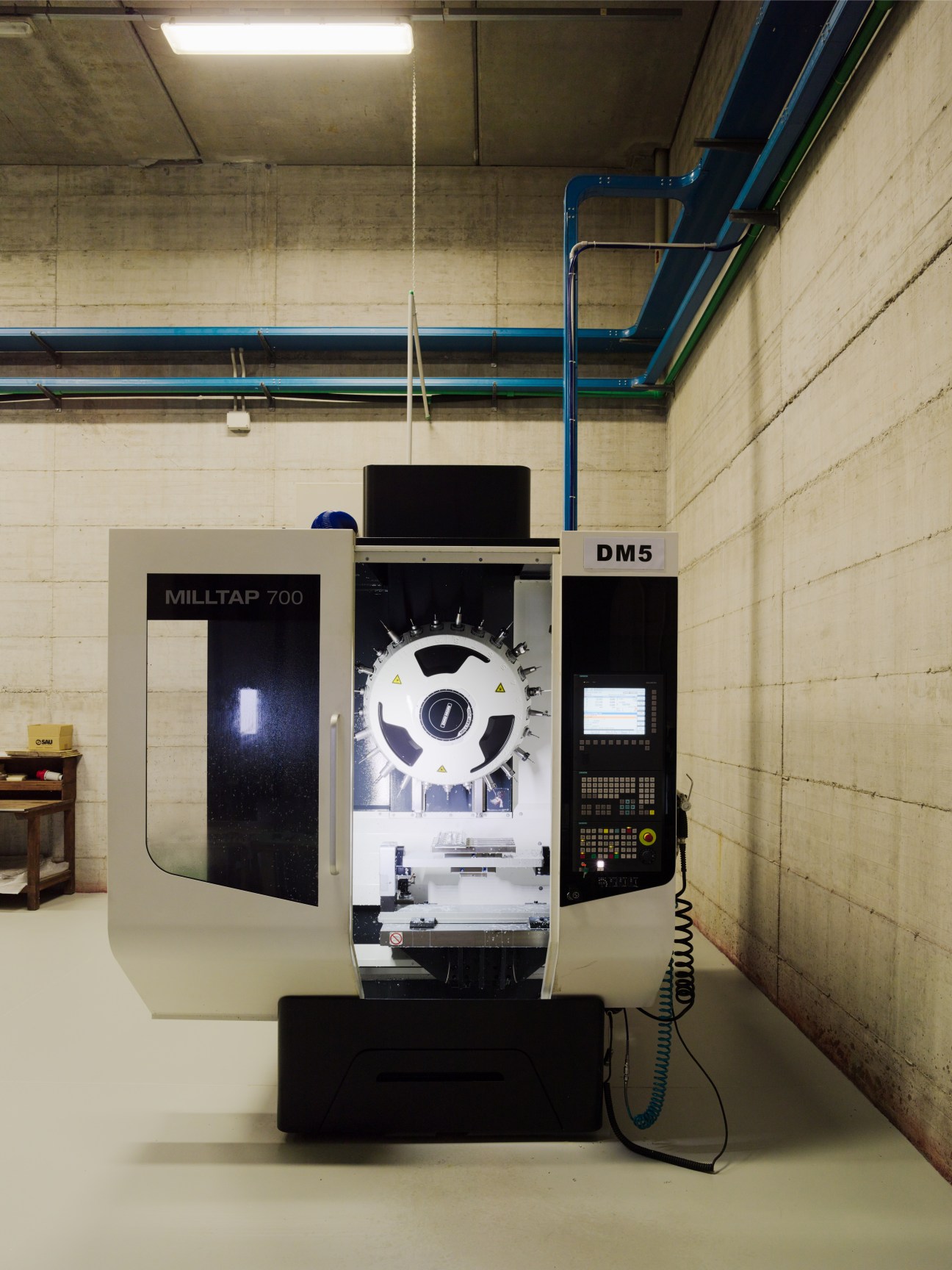 Industrial CNC milling machines in a factory production facility with concrete walls and blue overhead piping.