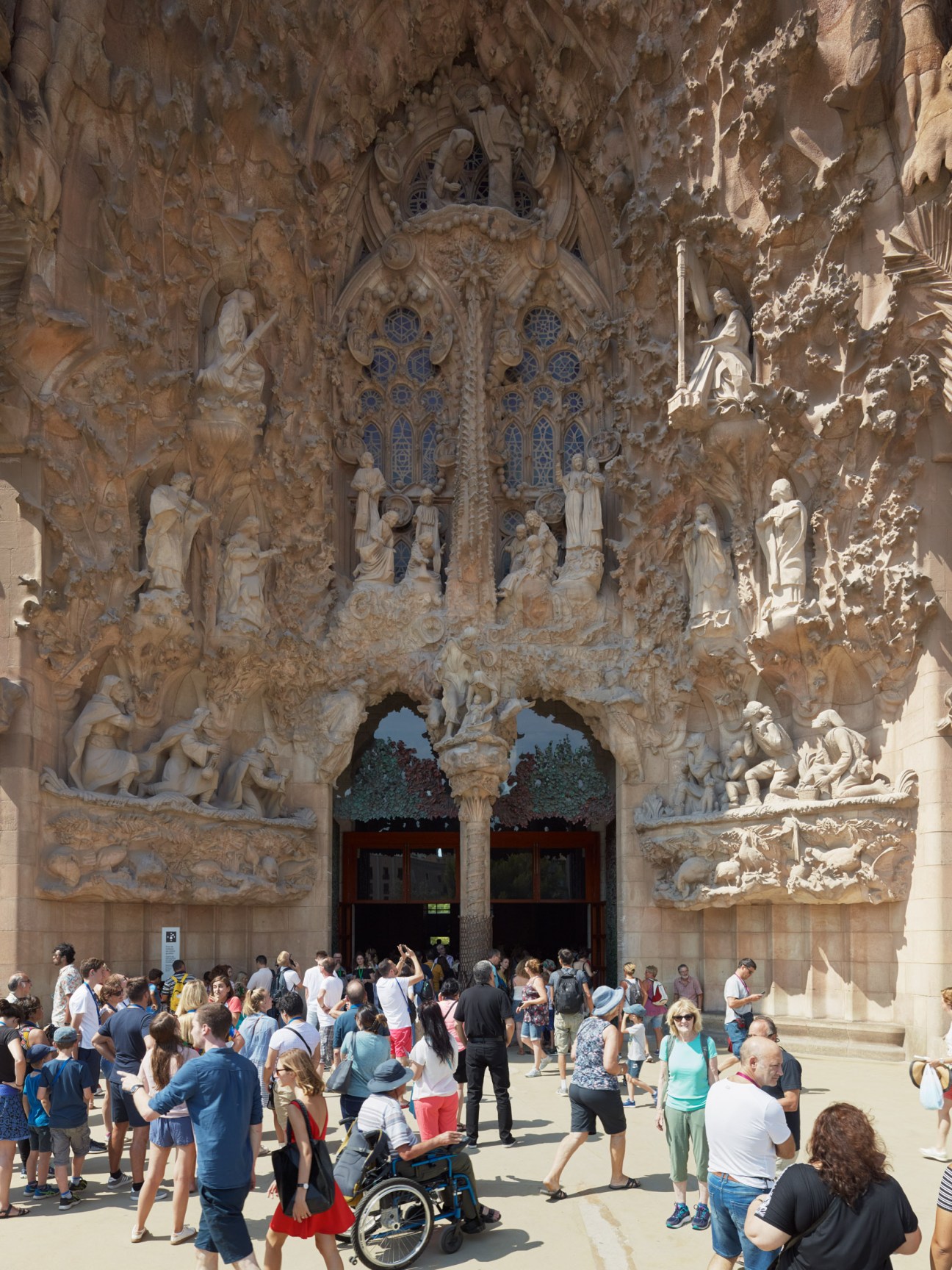 Intricate stone carvings of the Sagrada Família's Nativity façade with visitors gathered at the entrance below.