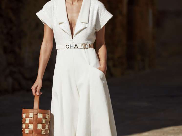 Model wearing a white Chanel dress with matching belt, brown woven Hereu bag and orange shoes.