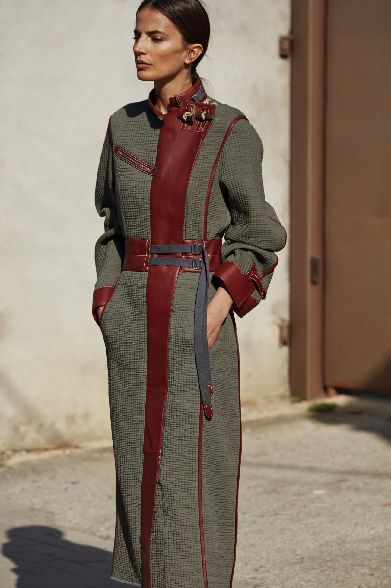 Woman wearing a long coat by Hermès in sage green and burgundy with leather trim details.