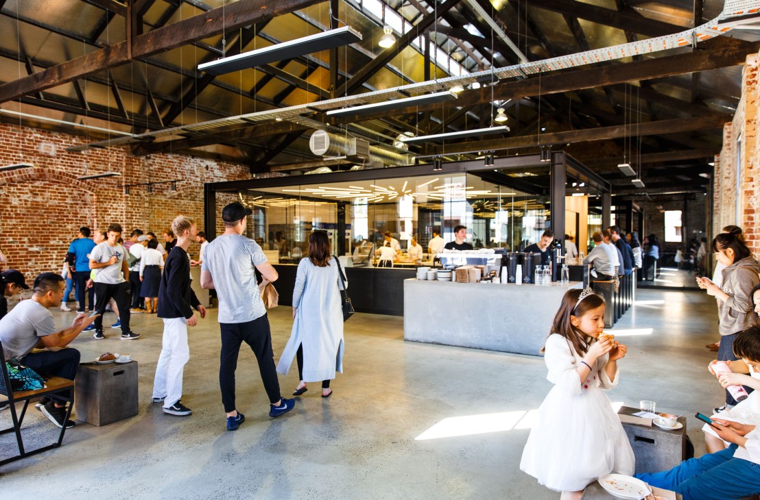 Interior of Lune bakery in Melbourne showing customers and staff in a converted warehouse with exposed brick and industrial ceiling.