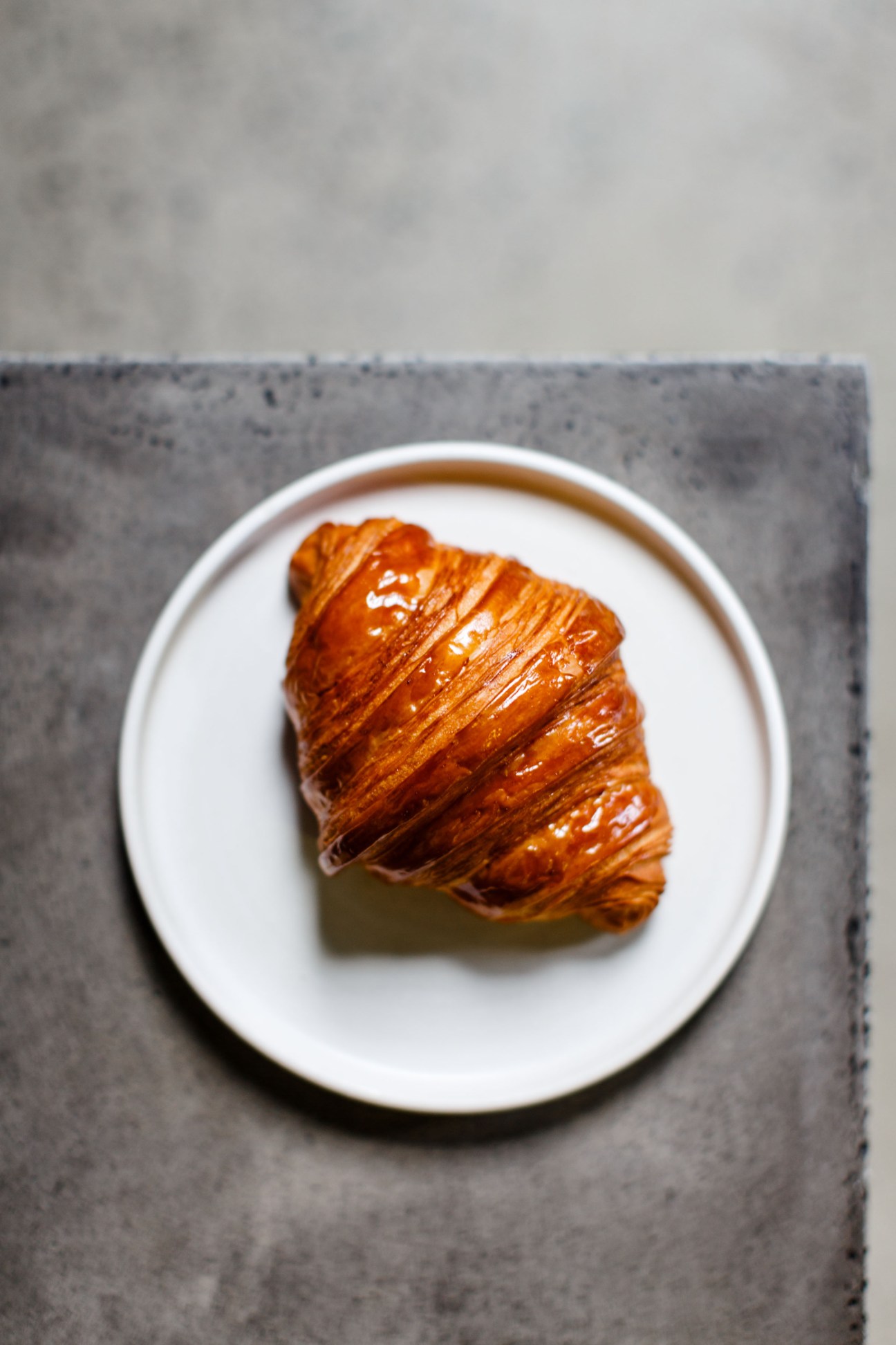 A golden, flaky croissant on a white plate atop a grey napkin.