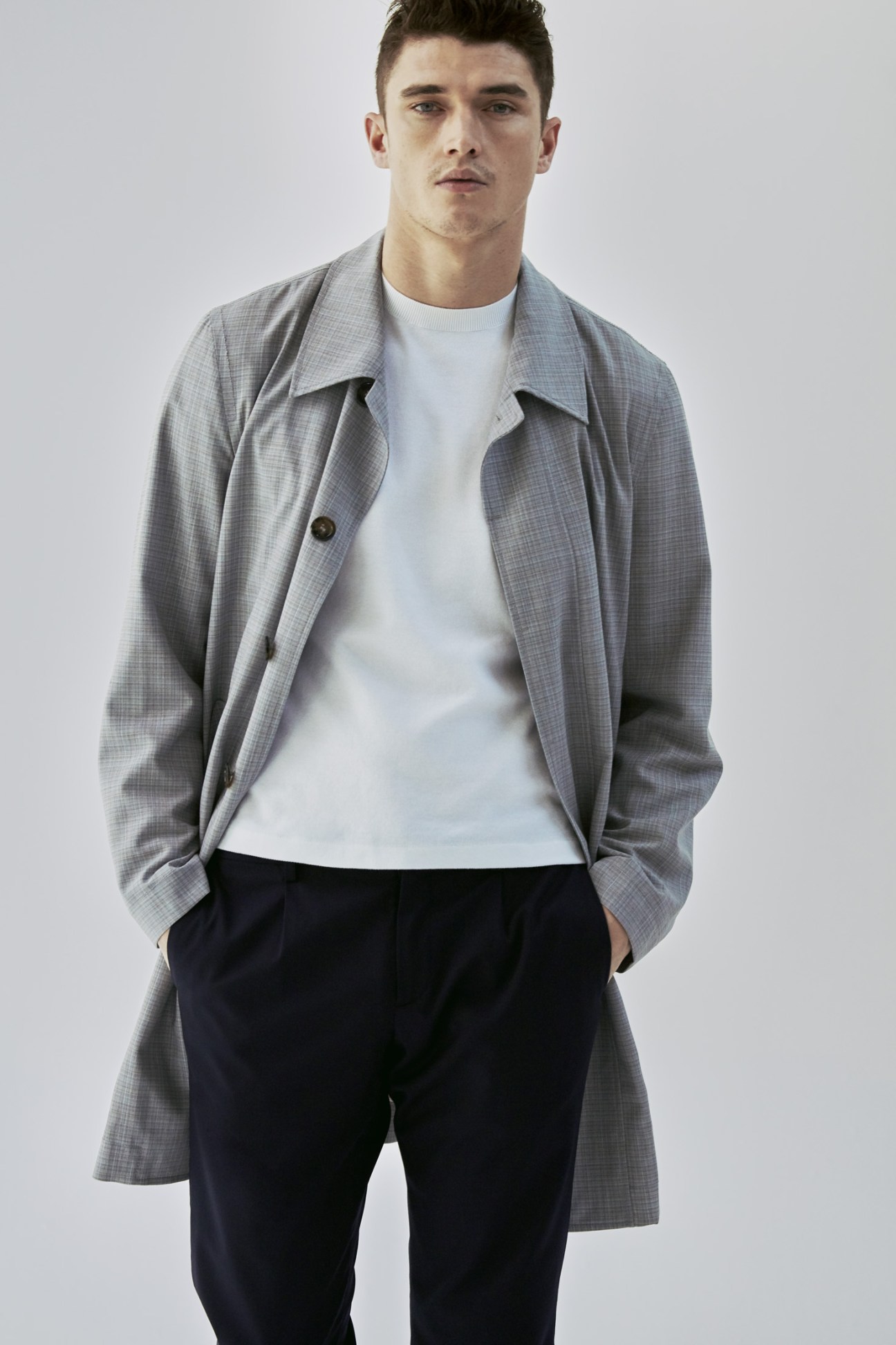 Male model wearing a grey checked coat by Canali over a white jumper and dark trousers.