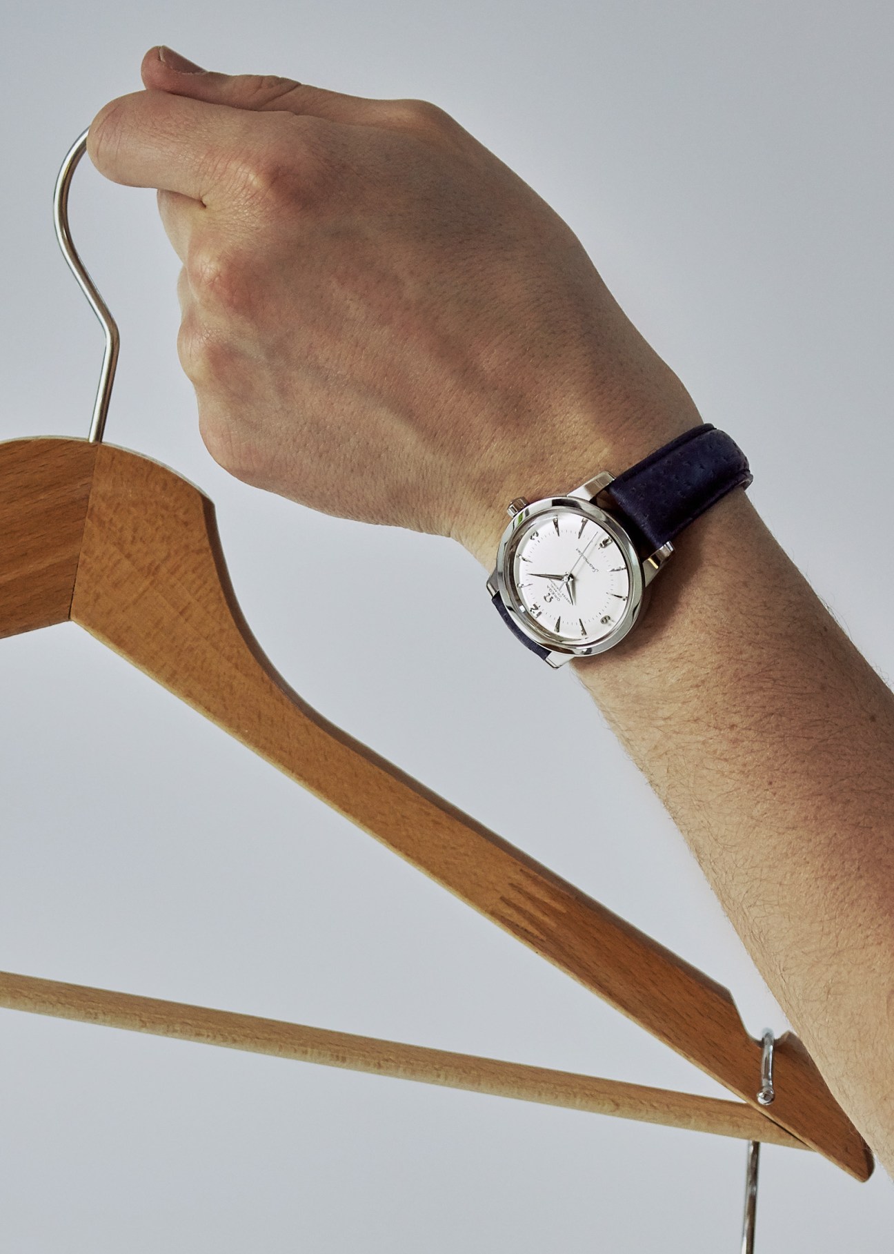 Omega watch with white dial and black leather strap on wrist holding wooden hanger.