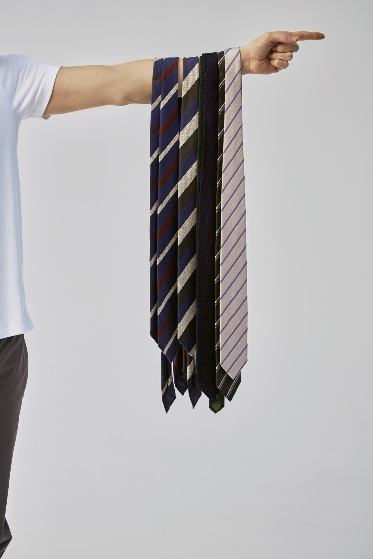 Hand holding seven striped ties in navy, black, and gray patterns by Drake's and Bigi Cravatte Milano.