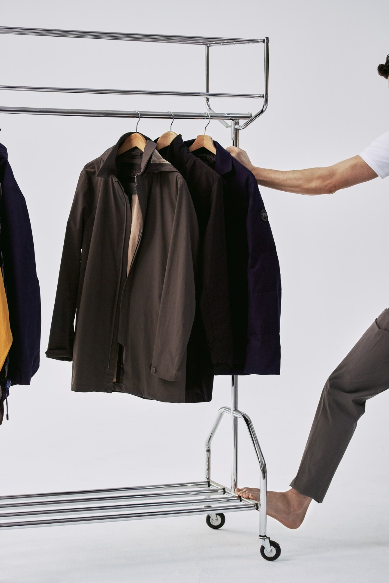 Three coats by Herno, Descente Allterrain, and Canada Goose hanging on a metal rack.