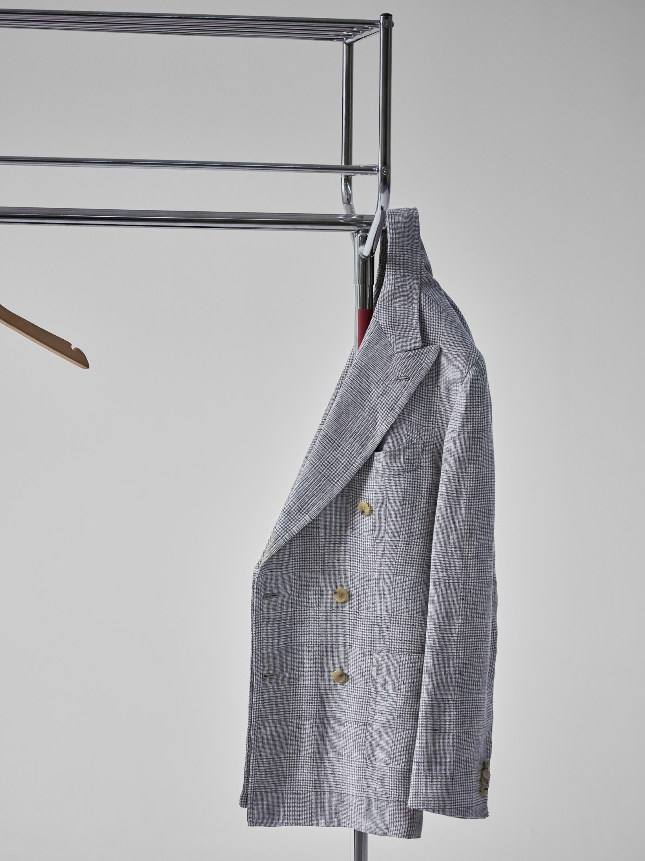 Gray checked blazer hanging on a chrome rail against a white background.