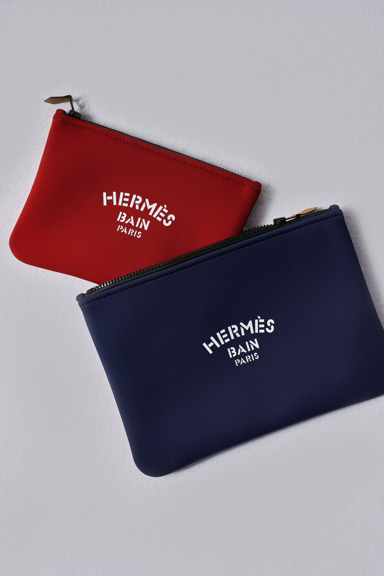Red and navy Hermès Bain Paris pouches with leather pull tabs displayed on white background.