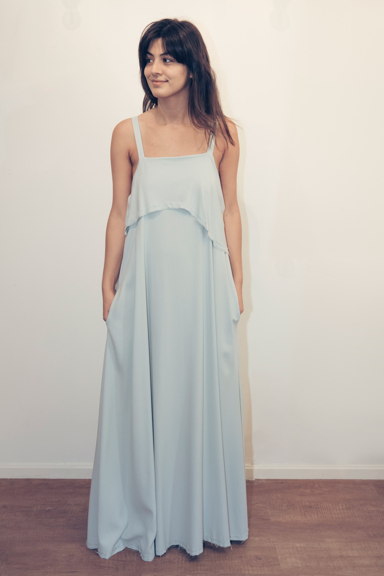 Woman wearing a light blue sleeveless dress with draped overlay designed by Luz Ballestero