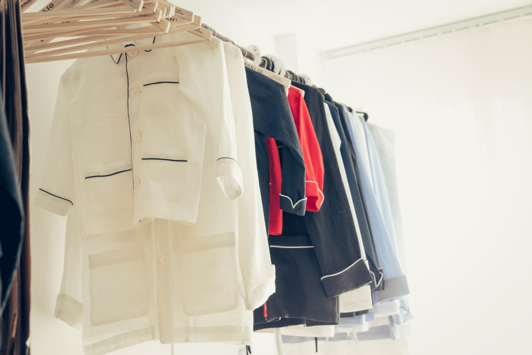 Carzoglio sleepwear collection displayed on wooden hangers, featuring navy and red piped linen pyjamas alongside white designs.