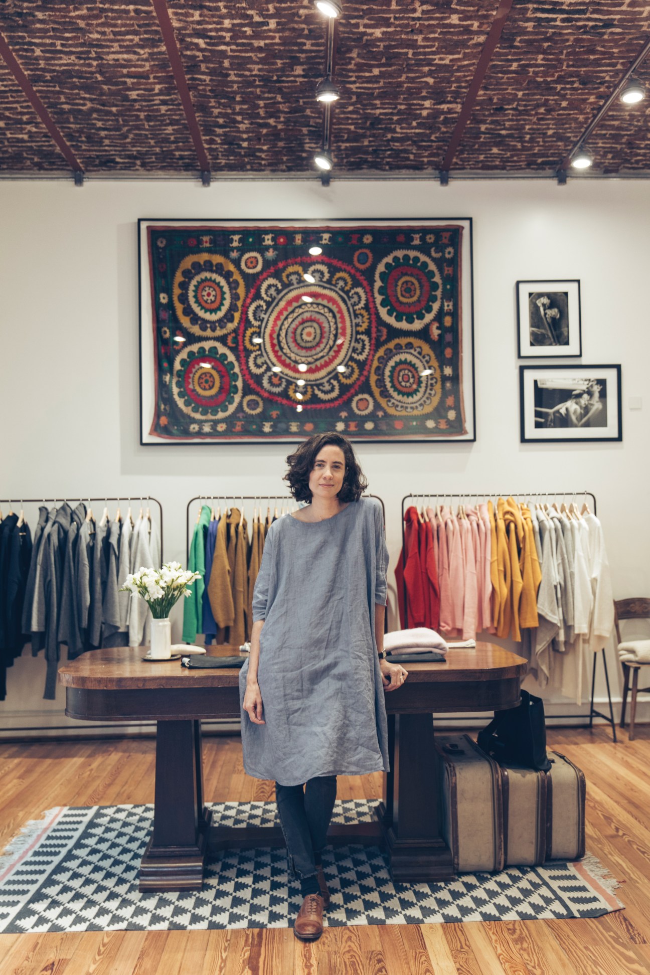 Cata Chavanne standing in her Blue Sheep knitwear showroom with colorful sweaters displayed on racks behind her.