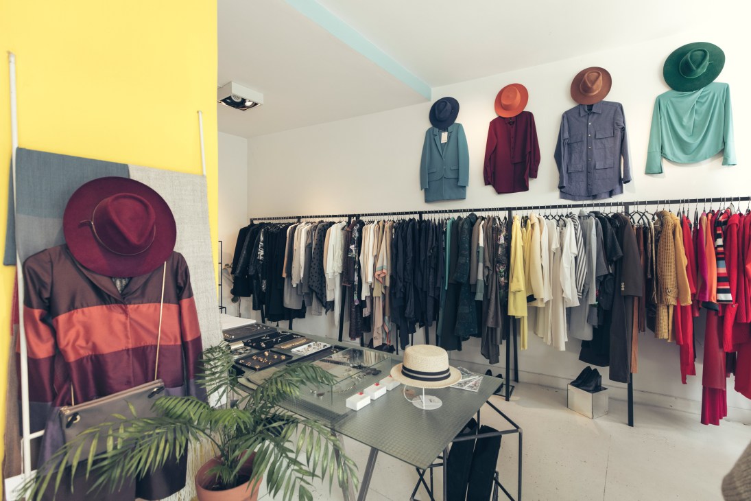 Interior of JT concept store in Palermo displaying clothing on racks and mannequins wearing colorful hats and jackets.