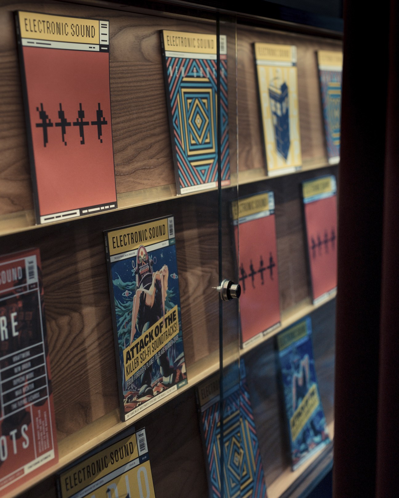 Display case of Electronic Sound magazines with colorful geometric cover designs on wooden shelves.
