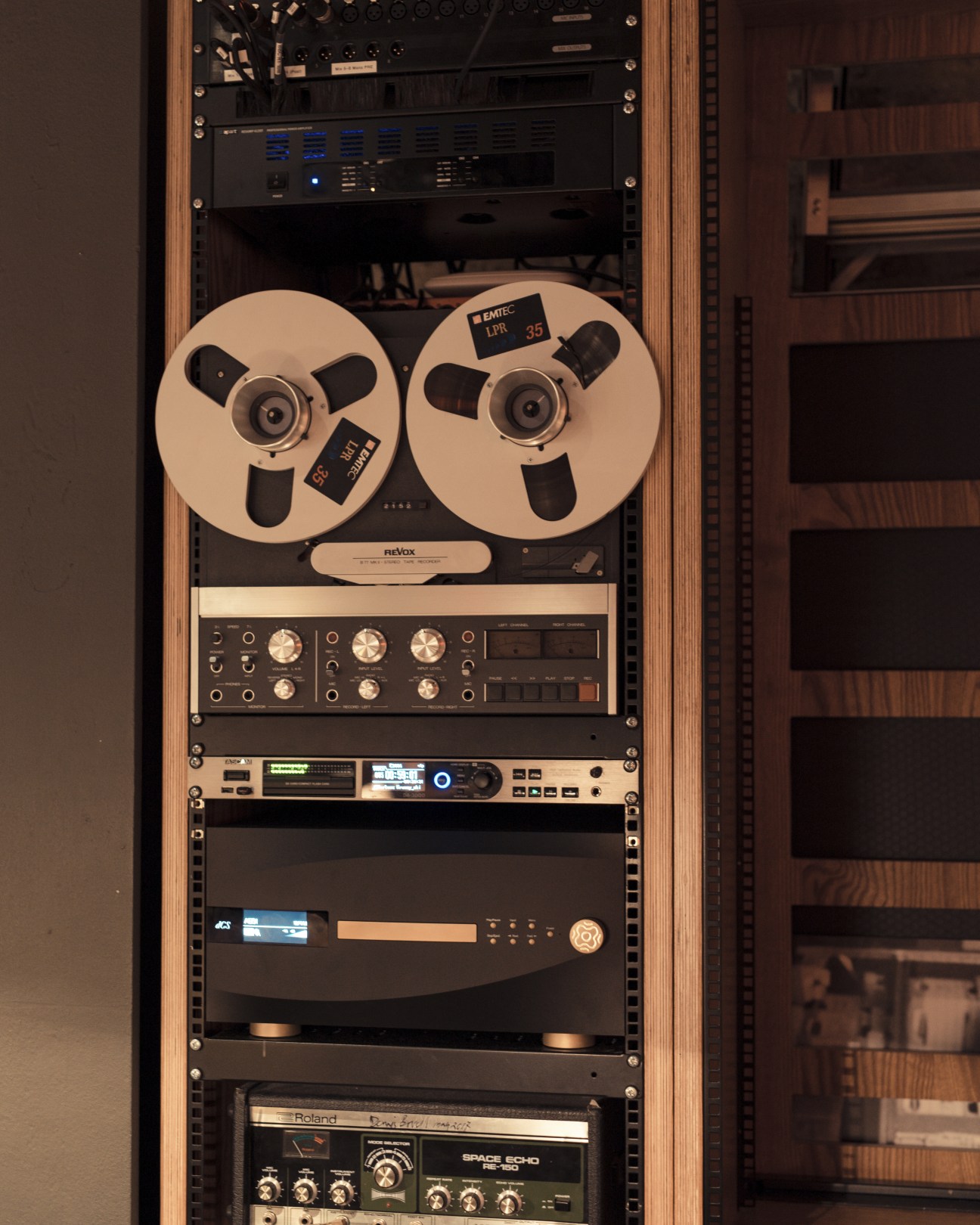 Professional audio equipment rack with reel-to-reel tape machine and electronic components in wooden frame.