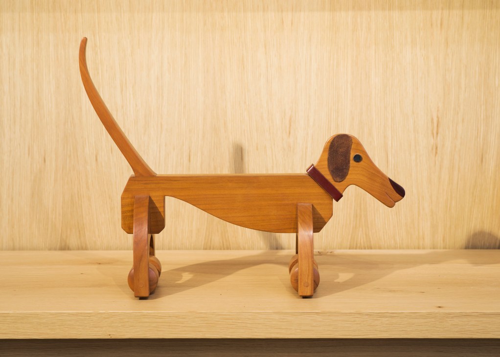 Wooden dachshund toy on wheels with brown and tan finish displayed on light wood surface.