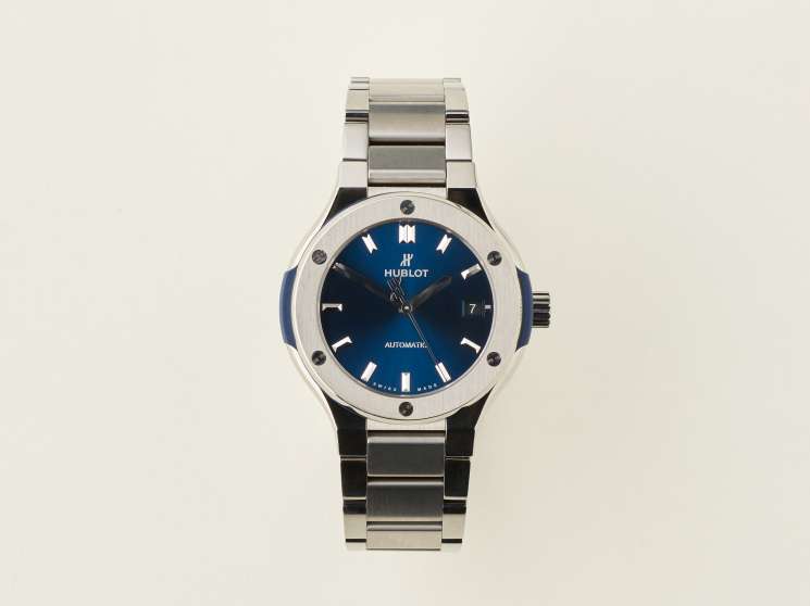 Hublot Classic Fusion titanium watch with blue dial and metal bracelet on cream background.
