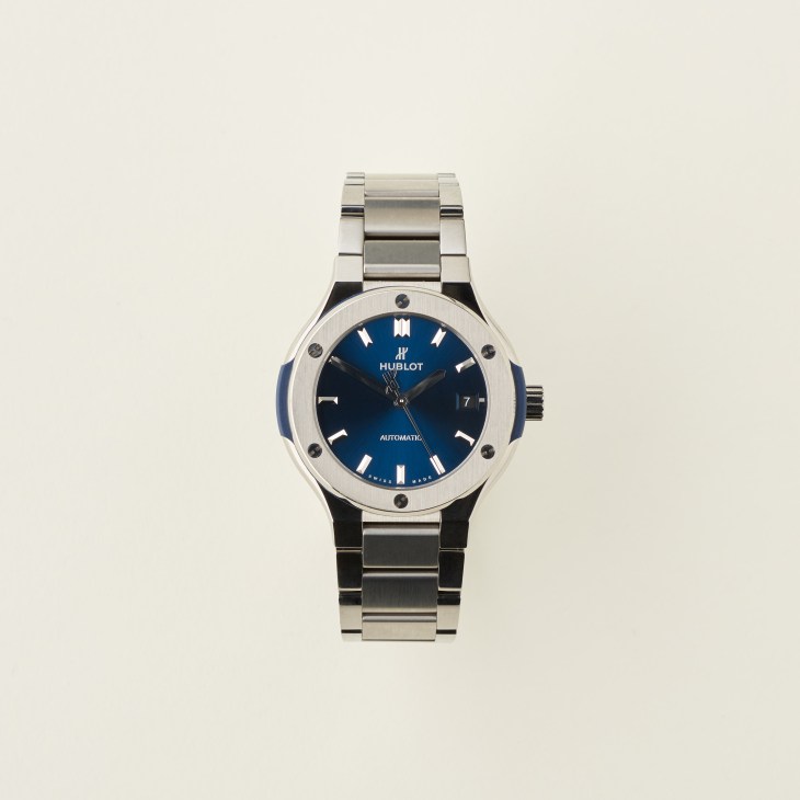 Hublot Classic Fusion titanium watch with blue dial and metal bracelet on cream background.
