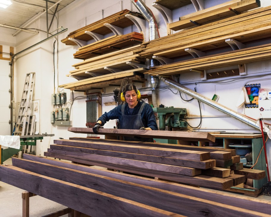 Heidi Earnshaw wearing yellow headphones and a navy apron works with wooden stacking pieces in a bright workshop.
