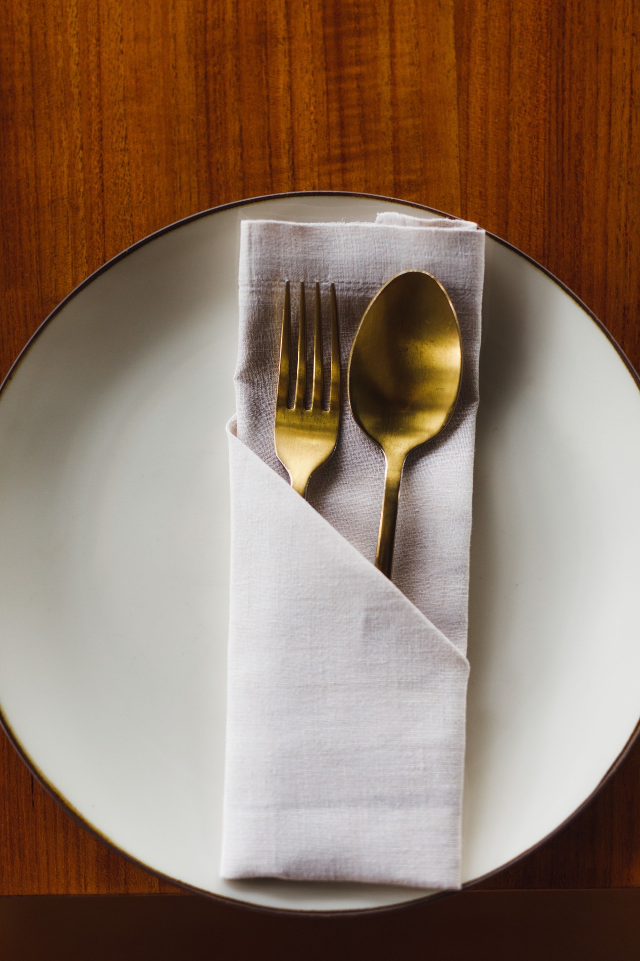Brass cutlery arranged on a white napkin placed on a plate with a wooden table background.