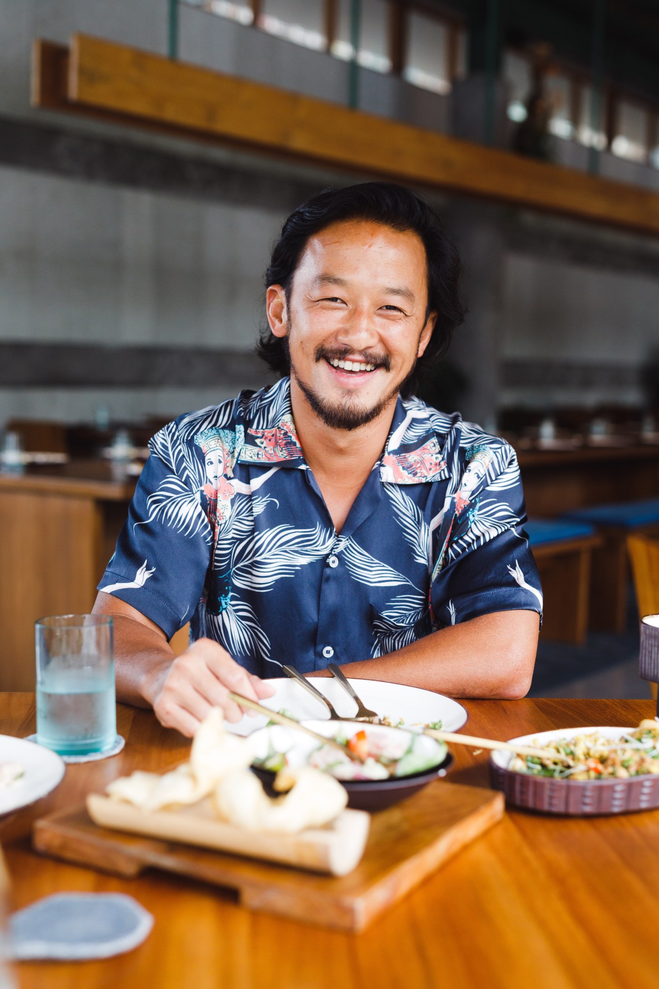 Ronald Akili, CEO of Potato Head, smiling at a wooden table in a restaurant setting