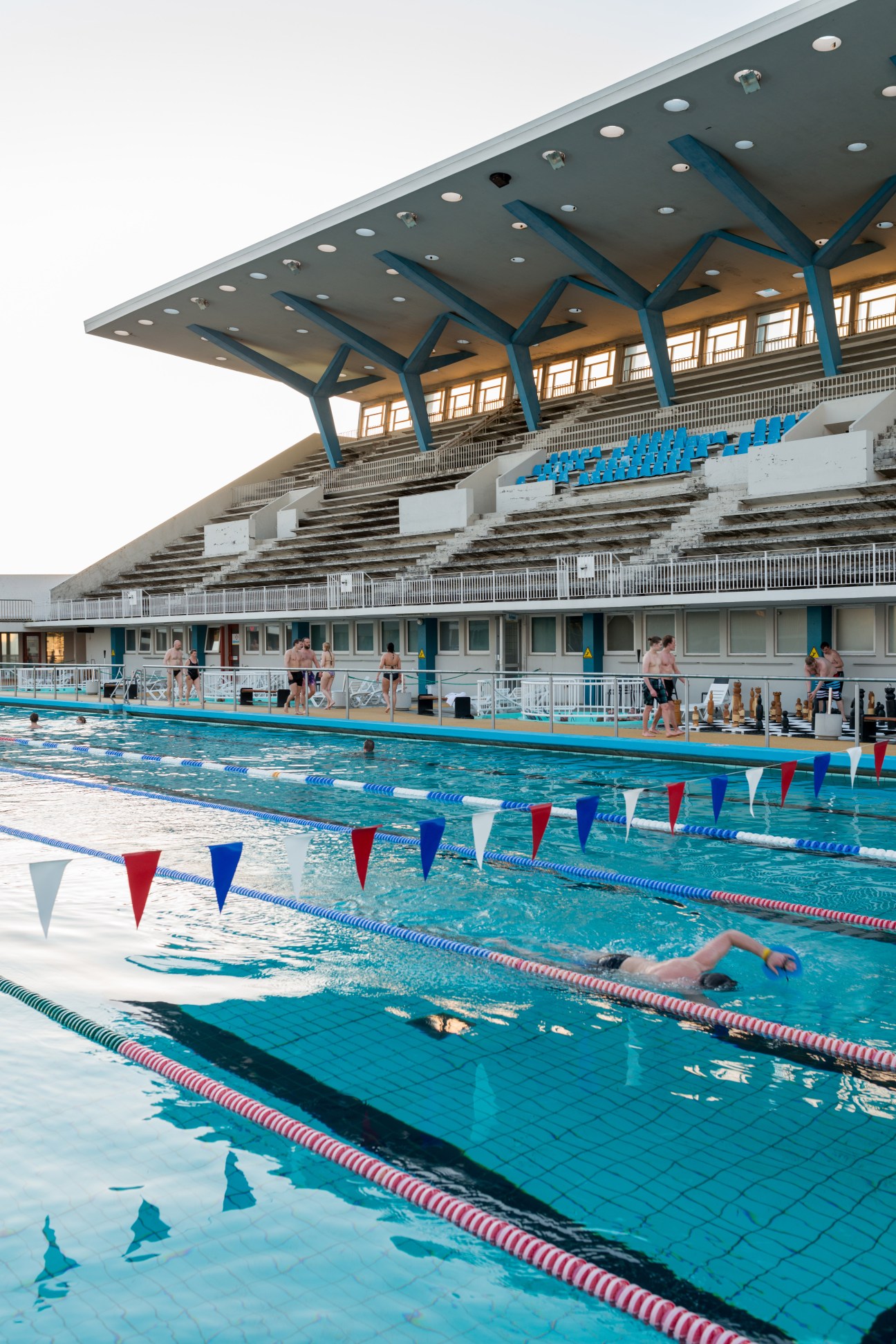 A swimmer doing laps in an outdoor pool at Laugardalslaug with lane dividers and spectator seating visible