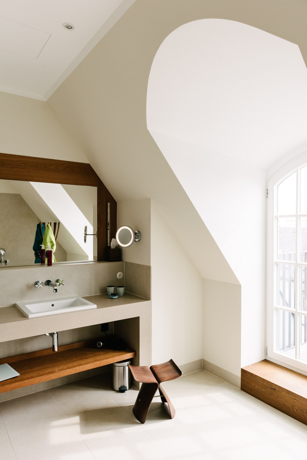 Spacious modern bathroom with Sori Yanagi butterfly stool, wood vanity, and curved white sculptural element.