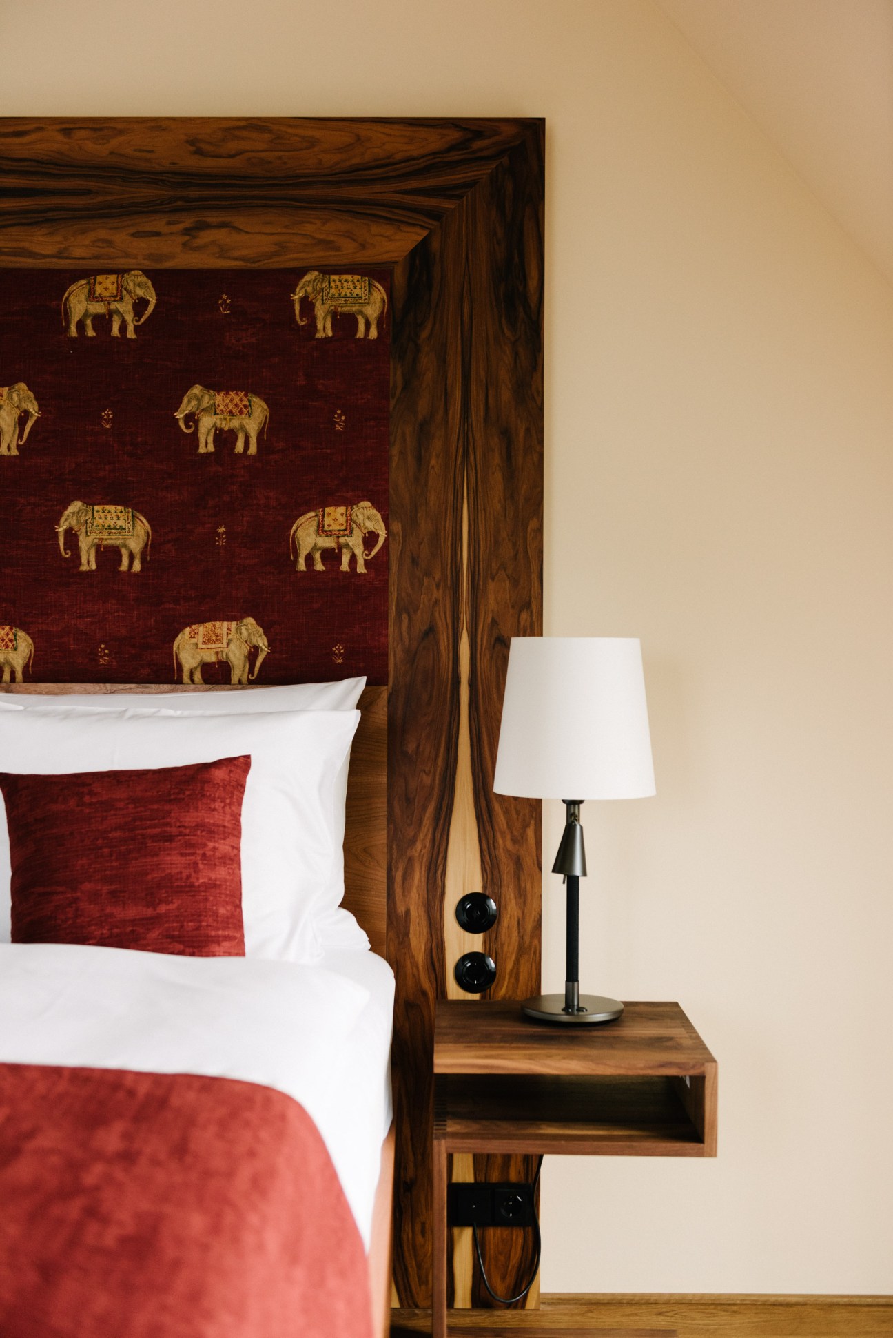 Wooden bed headboard with burgundy fabric featuring gold elephant motifs and white pillows.