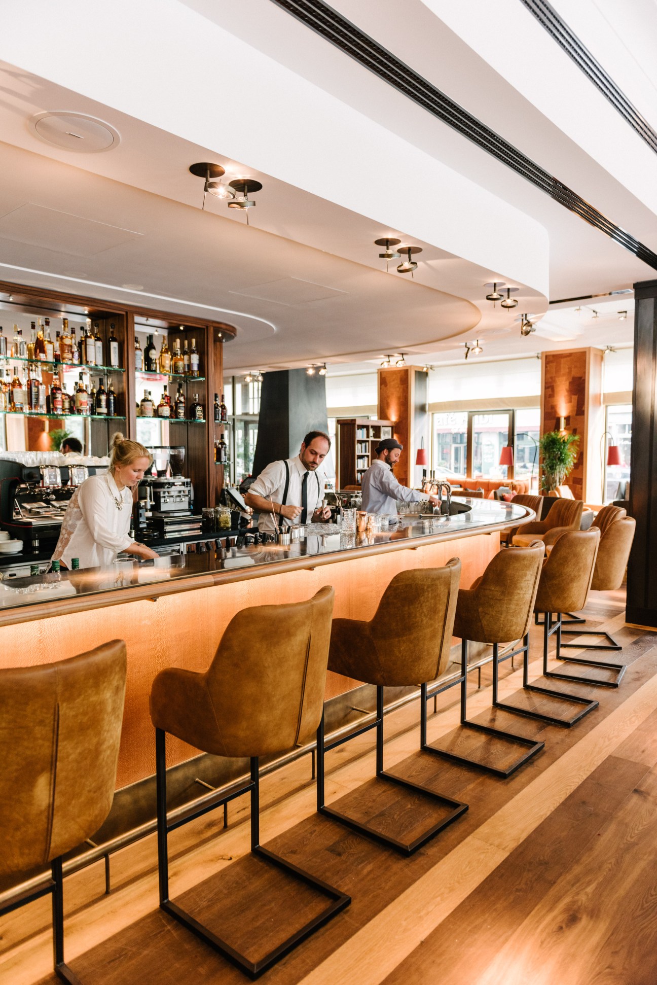 Orania Berlin lobby bar with bartenders behind curved counter and tan leather bar stools.