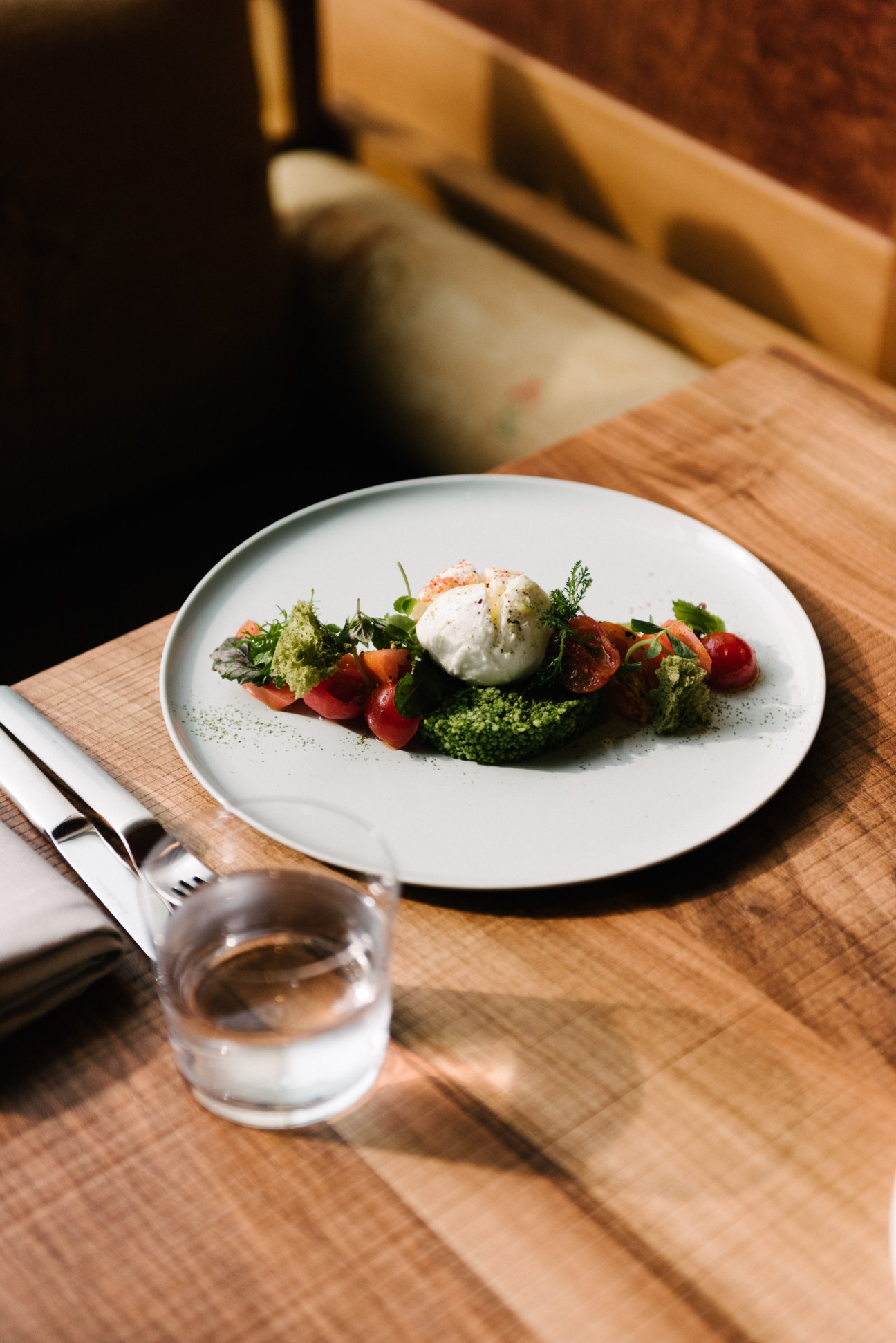 A plated dish from chef Philipp Vogel's kitchen at Orania Berlin featuring a burrata-like cheese, fresh vegetables and green sauce.