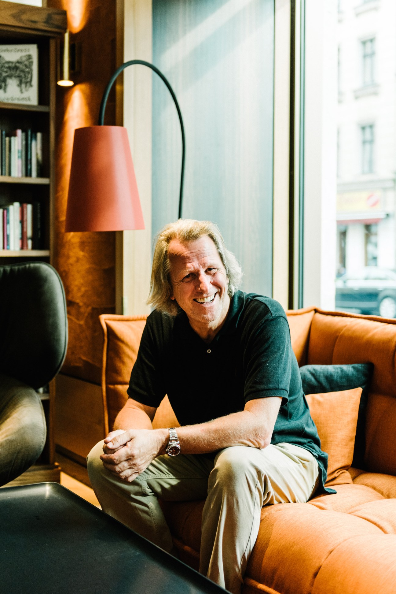 Dietmar Müller-Elmau seated on an orange sofa in the Orania Berlin hotel lobby.