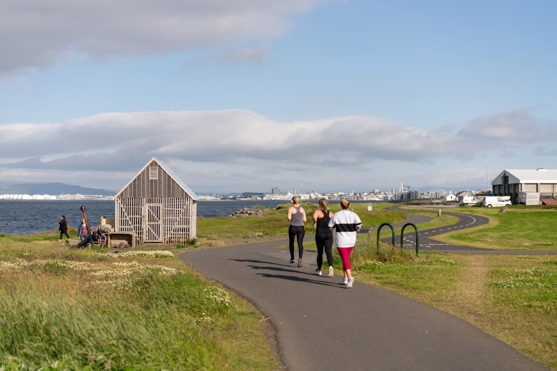 Three people jogging on a coastal path with wooden structures and ocean view