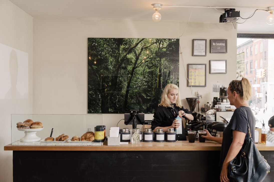 A barista with blonde hair serves coffee at the Saturdays NYC espresso bar counter.
