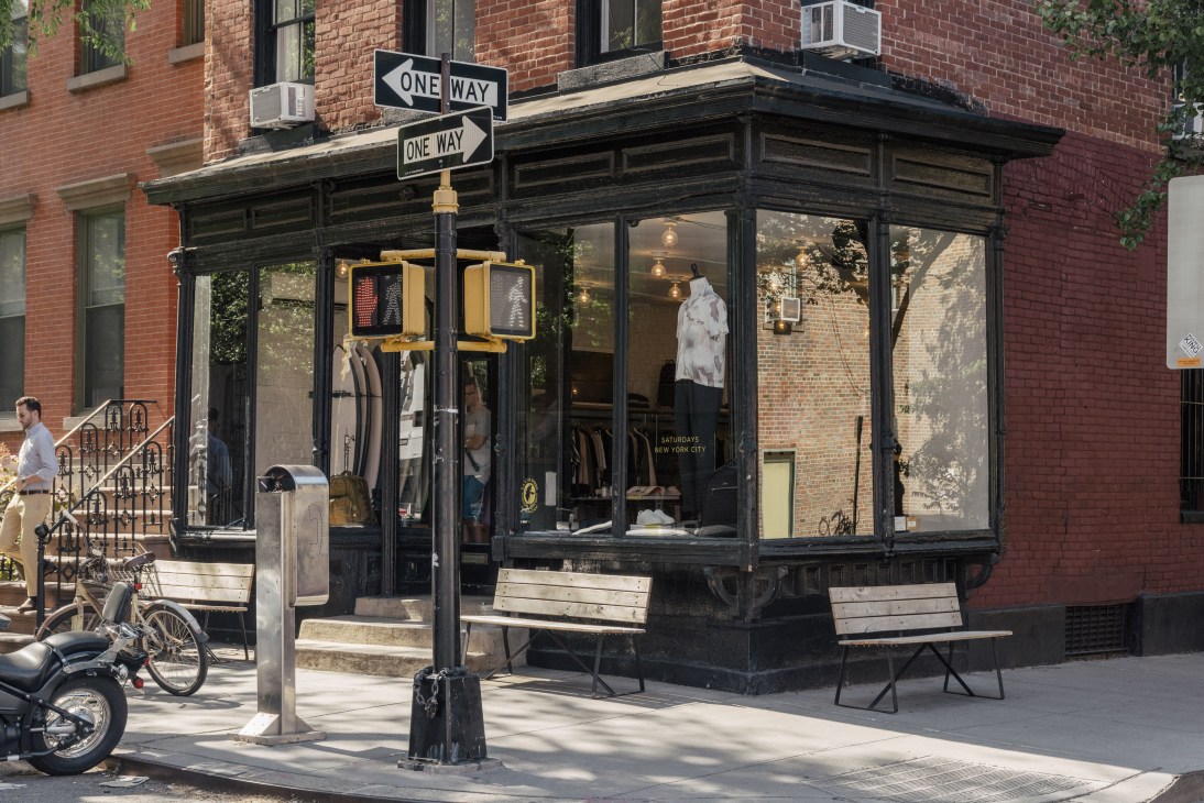 Saturdays NYC storefront on Crosby Street with black storefront, large windows displaying clothes, and one-way street signs above.