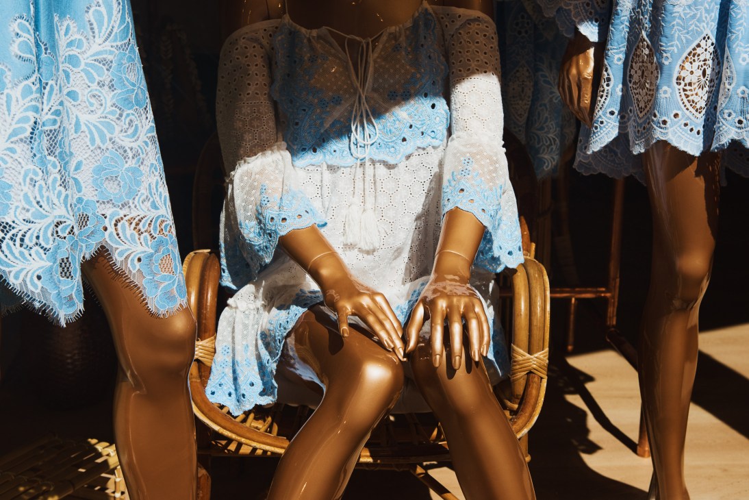 Gold mannequins wearing blue and white lace summer clothing displayed in bright sunlight.