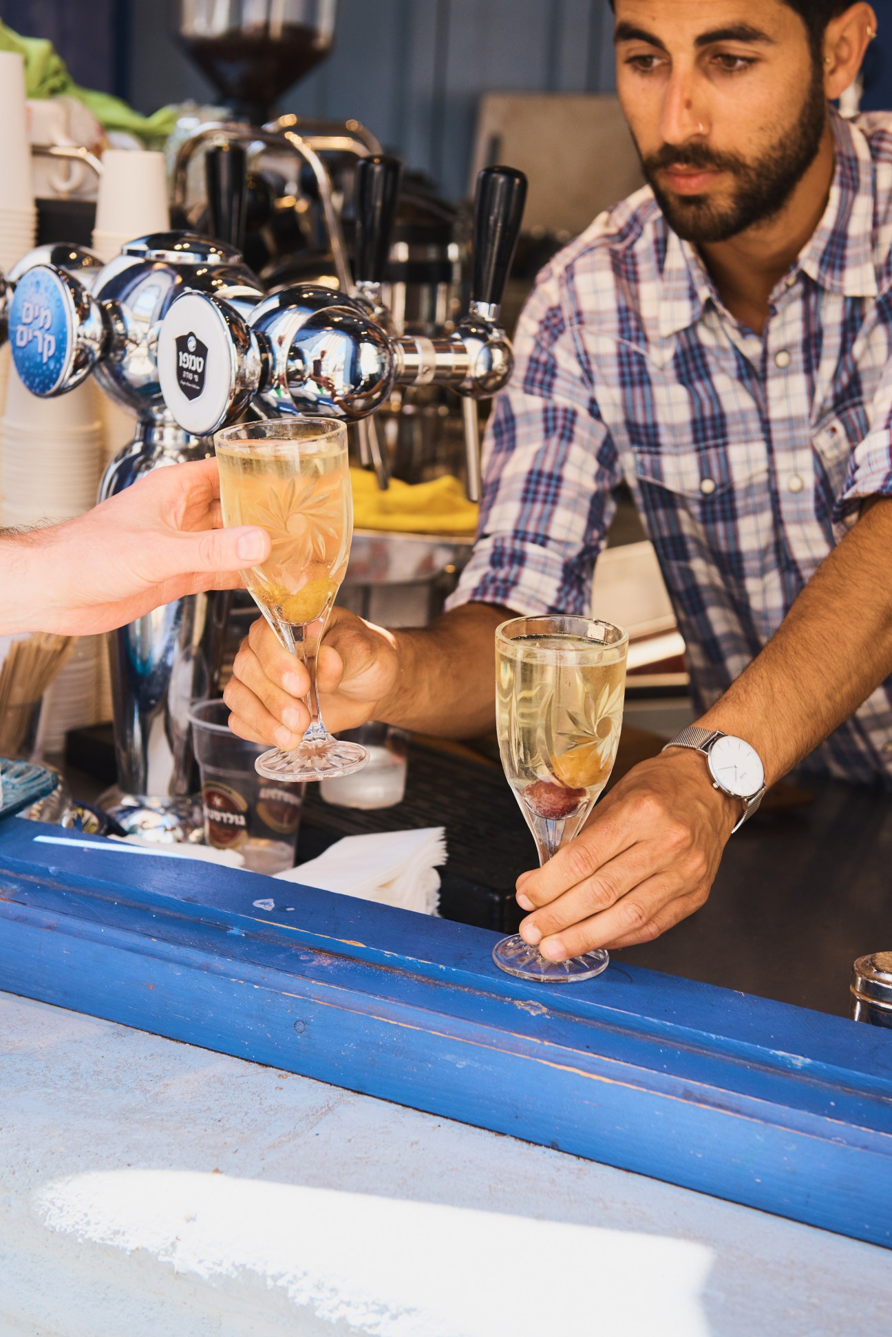 Bartender in checkered shirt pouring a sparkling drink at a bar with beer taps.