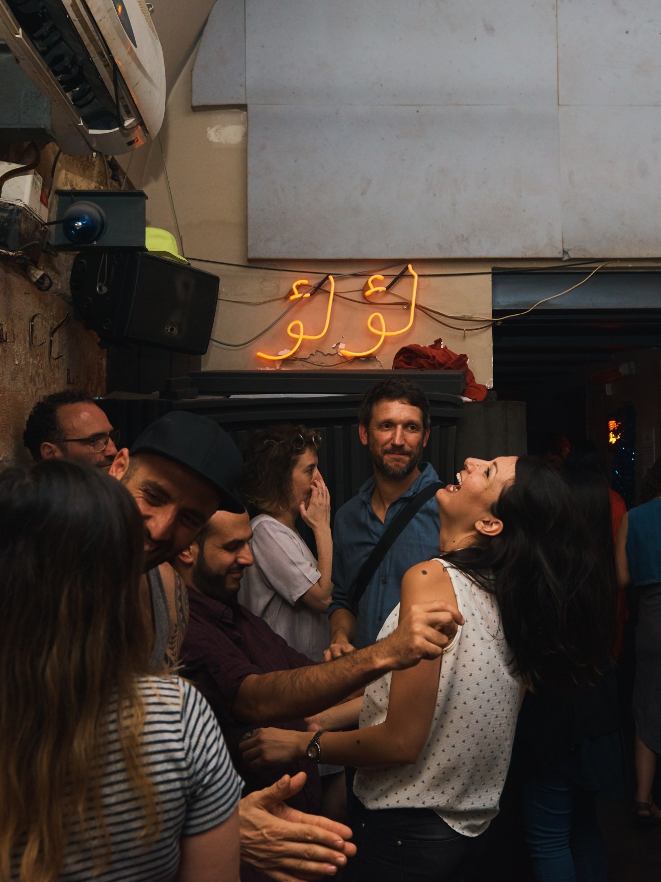 People dancing together inside Anna Loulou bar with glowing neon sign visible above
