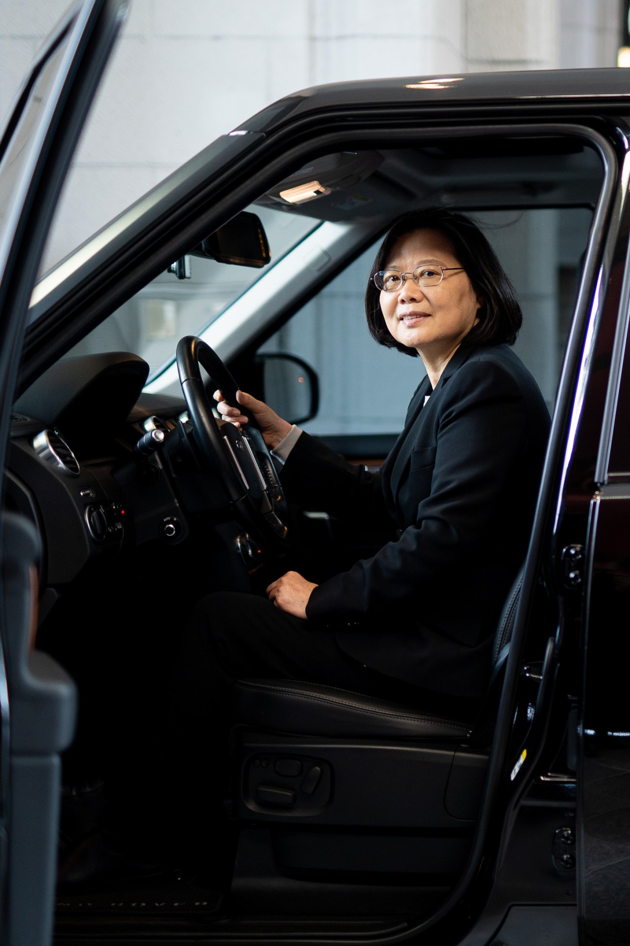 Taiwan's president Tsai Ing-wen sits in the driver's seat of a car, wearing glasses and a dark blazer.