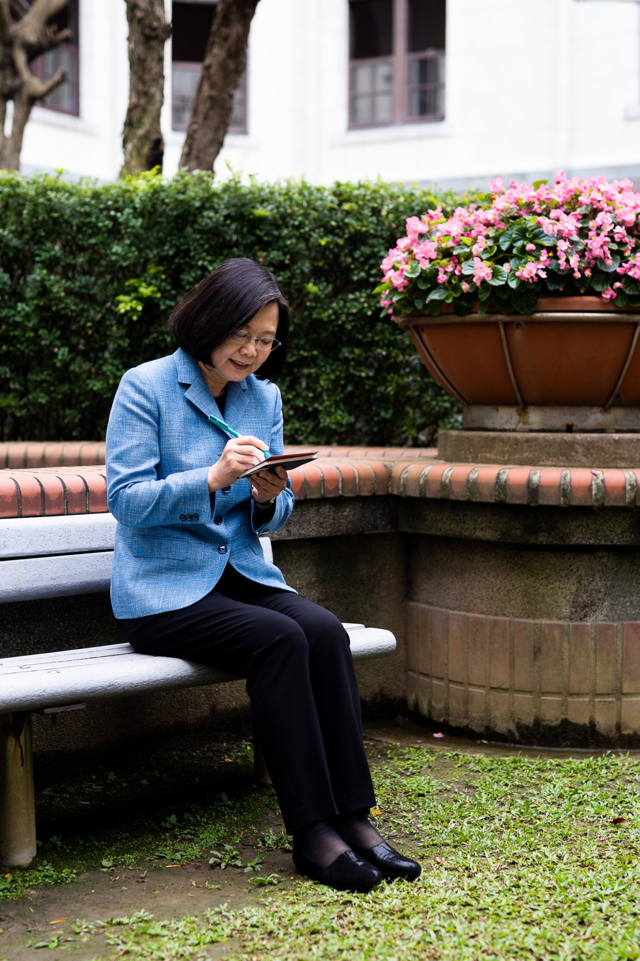 Taiwan President Tsai Ing-wen sits in a courtyard garden holding a tablet, wearing a blue blazer.