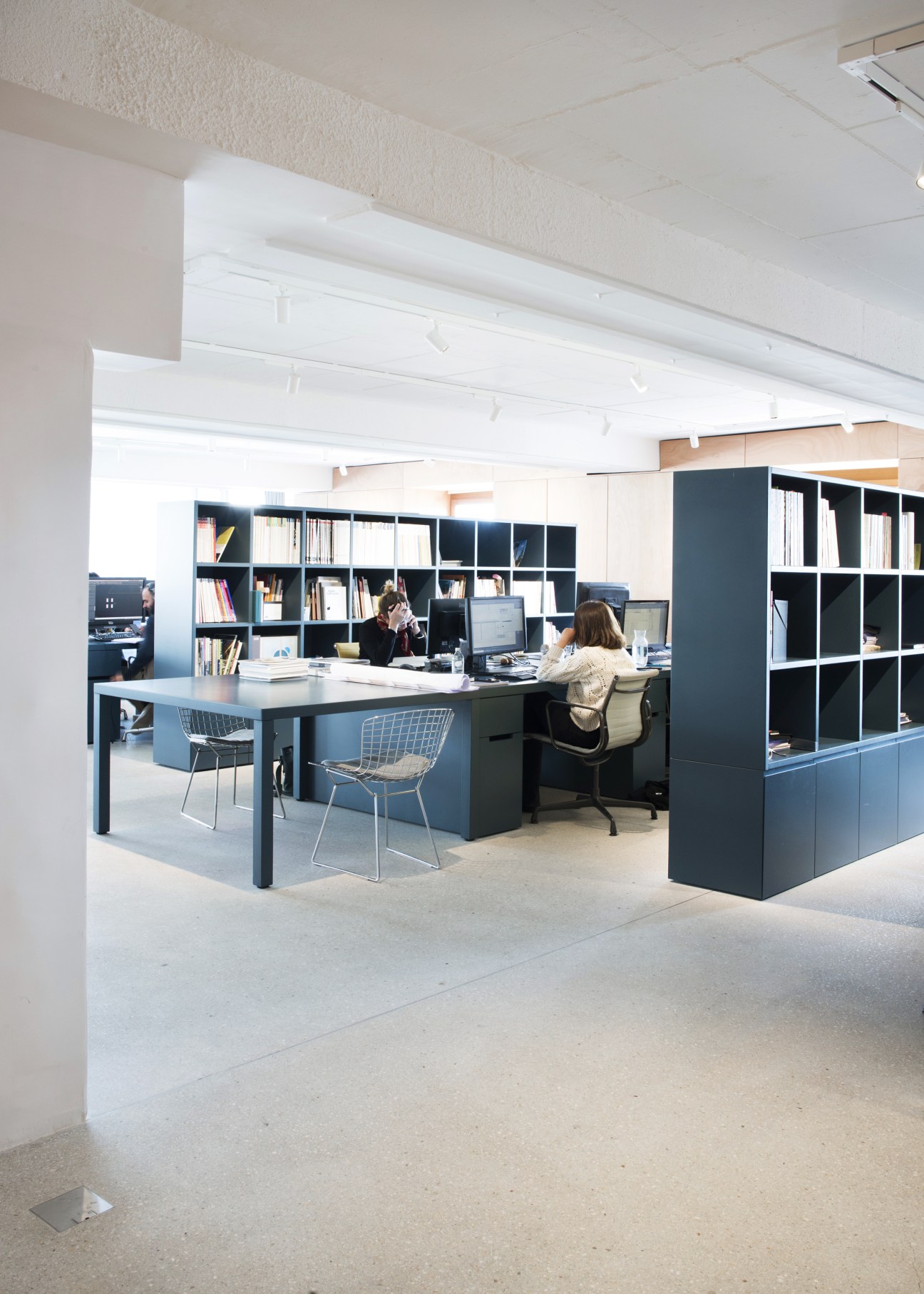 Modern office space with Eames wire chairs at desks beside modular black storage units and shelving.