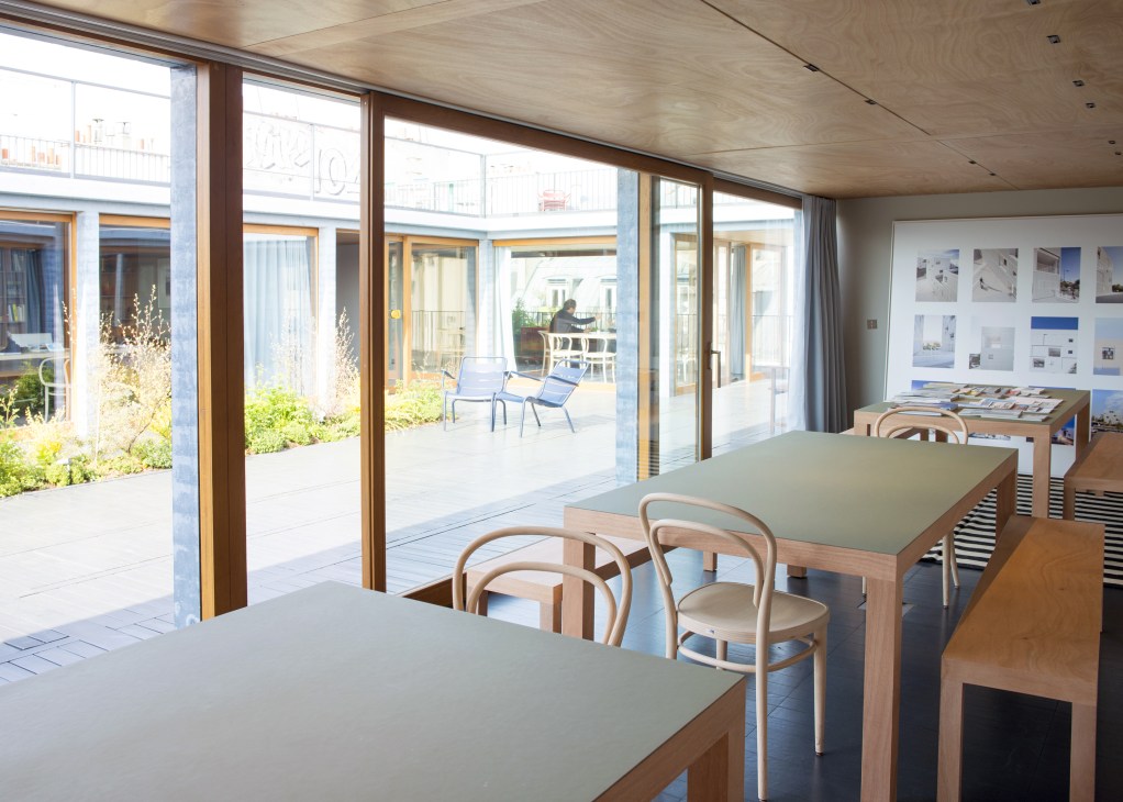 Modern dining area with wooden tables and Thonet 209 bentwood chairs overlooking a courtyard with large windows.