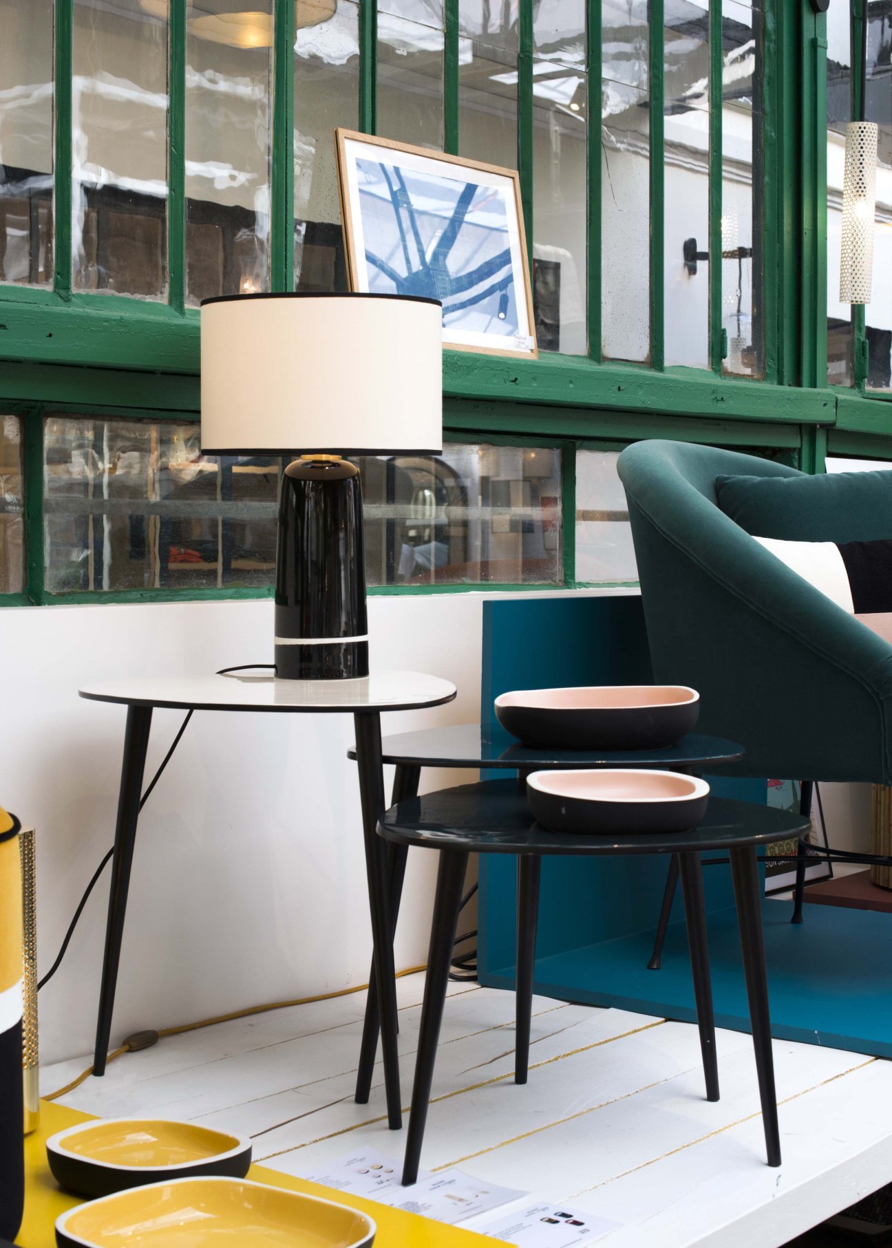 Sarah Lavoine showroom displaying oval tables with black legs, lamp, teal chair and ceramic dishware