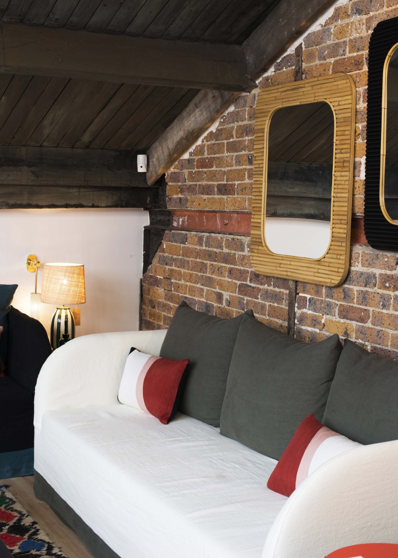 Mid-century modern wooden mirror with rounded frame mounted above a white bed with colorful pillows in an industrial brick bedroom.